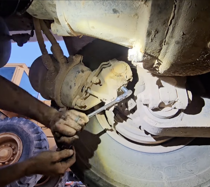 Mechanic using a wrench to service brake components under a commercial truck